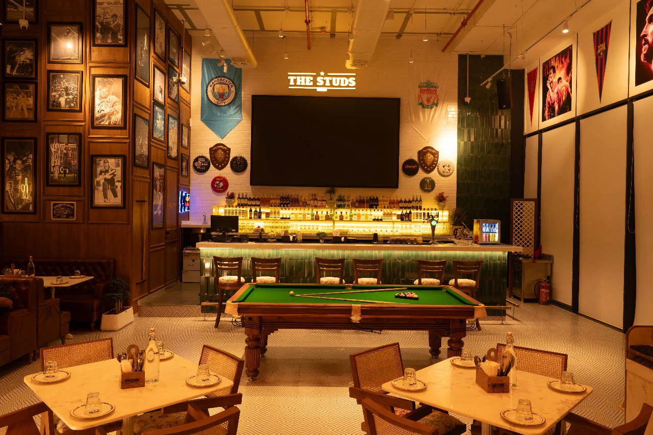 The main bar area and a pool table at The Studs, a sports-themed hospitality interior design project in Pune, with walls decorated with sports memorabilia.