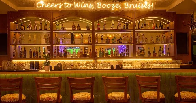 The illuminated bar counter with a neon sign that reads 'Cheers to Wins, Booze, Bruises' at The Studs - Sahakar Nagar.