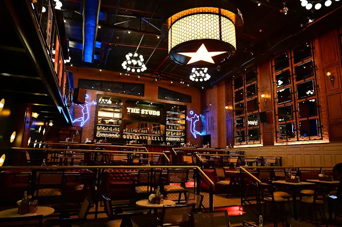 A wide shot of The Studs sports bar in Ranchi, highlighting the impressive central light fixture, multi-level seating, and the main bar.