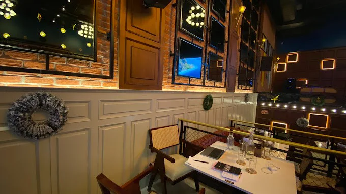 Close-up of a seating nook at The Studs - Ranchi, showing the mix of brick and wainscoting paneling, cane chairs, and decorative lighting.