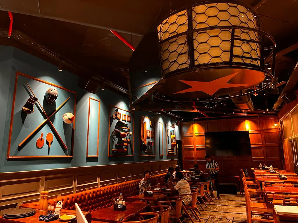 The main dining area of The Studs sports bar in Vashi, showcasing the unique star-shaped light fixture and custom sports-themed wall art.