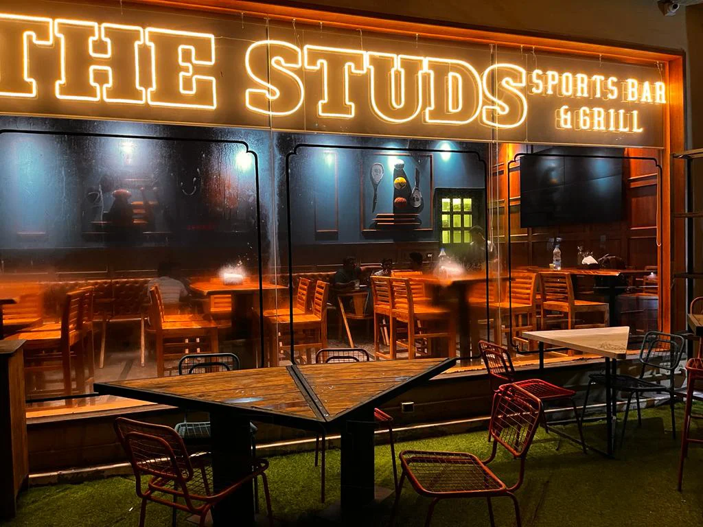 The exterior view of The Studs in Vashi, highlighting the prominent 'The Studs Sports Bar & Grill' neon sign and outdoor seating.