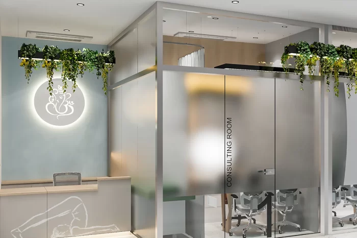 Clinic consulting room entrance with frosted glass partition, modern Ganesha logo light, and wood reception desk.